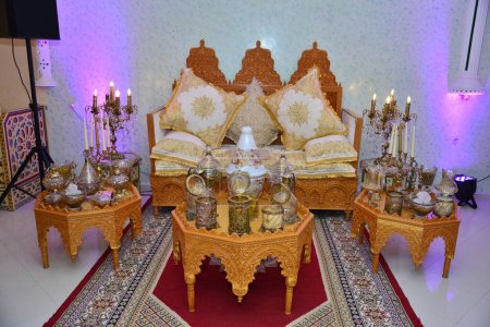 Eine elegant inszenierte Hochzeit im traditionellen marokkanischen Stil mit großem Sofa, auf dem das Brautpaar sitzt und den Segen der Gäste entgegennimmt, umgeben von wunderschönem Blumendekor und Kerzenständern