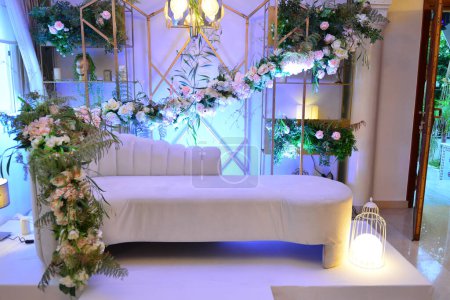 Photo for An elegantly staged traditional morocco style wedding with large sofa for the wedding couple to sit and receive blessings from the guests, surrounded by beautiful floral decor and candle light stands - Royalty Free Image