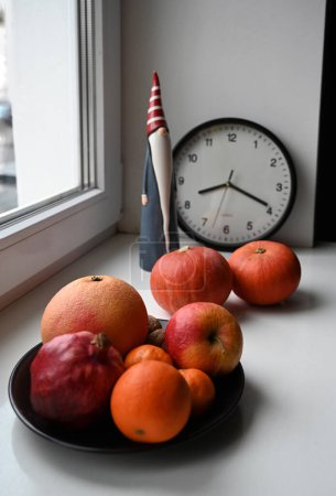 Foto de Reloj, un plato de frutas, calabazas y Santa Claus figura en el alféizar de la ventana - Imagen libre de derechos