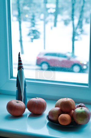 Téléchargez les photos : Une assiette de fruits, citrouilles et Père Noël figure sur le rebord de la fenêtre - en image libre de droit