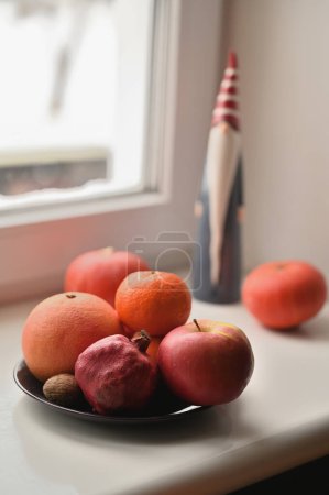 Foto de Un plato de frutas, calabazas y santa claus figura en el alféizar de la ventana - Imagen libre de derechos