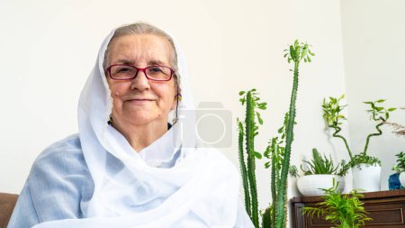 Foto de Retrato de una anciana musulmana de ochenta años con hiyab blanco sentada en casa mientras ayunaba durante el mes de Ramadán. - Imagen libre de derechos