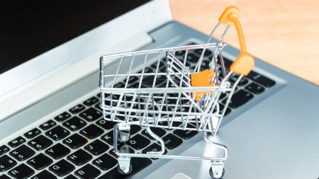Online-Einkaufskonzept. Warenkorb oder Einkaufswagen und Laptop auf Holztisch
