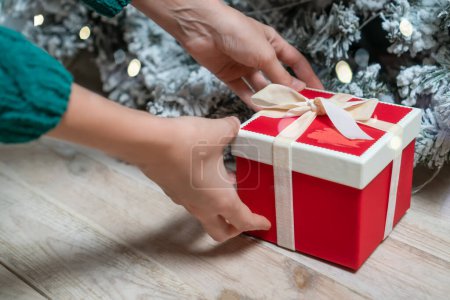 Foto de Las manos de las mujeres en un suéter verde toman o ponen una caja de regalo roja debajo del árbol de Navidad. Concepto de Navidad y Año Nuevo - Imagen libre de derechos