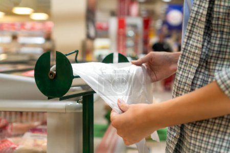 Primer plano de las manos de las mujeres arrancando una bolsa de celofán biodegradable para empacar en una tienda de comestibles