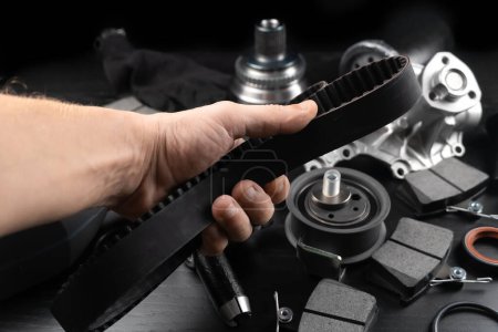 Timing belt and tension rollers of gas distribution system of car engine, concept of car maintenance. Master's hand holds timing belt against background of spare parts.