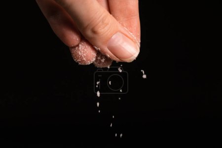 Foto de Los dedos femeninos espolvorean sal sobre un fondo negro, copian el espacio. Macrofotografía - Imagen libre de derechos