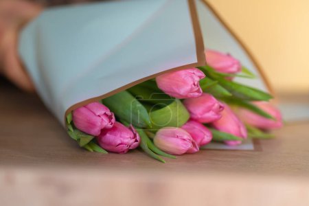 Téléchargez les photos : Gros plan d'un fleuriste recueillant un bouquet de tulipes roses sur une table, mise au point sélective - en image libre de droit