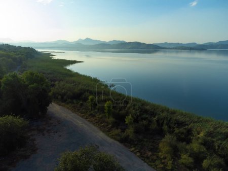 Téléchargez les photos : Vue par drone de la rive du lac surplombant les montagnes à l'aube. Beau paysage d'été avec lac et montagnes. Village de pêcheurs en Turquie. - en image libre de droit