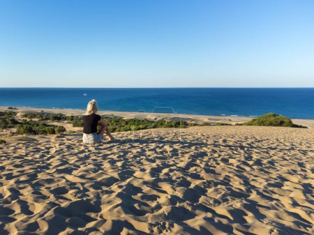 Téléchargez les photos : Vue par drone d'une jeune femme assise sur des dunes de sable sur la belle plage de Patara sur la côte méditerranéenne. Soif d'errance, regard solitaire sur la mer. - en image libre de droit