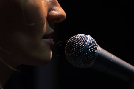 Téléchargez les photos : Gros plan du microphone et d'une partie du visage d'une jeune chanteuse sur fond noir - en image libre de droit