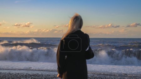 Téléchargez les photos : Vue arrière de la femme en manteau debout devant la mer.Homme triste et émotionnel regardant au loin. Navire à l'horizon. - en image libre de droit