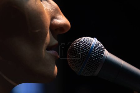 Téléchargez les photos : Gros plan du microphone et d'une partie du visage d'une jeune chanteuse sur fond noir - en image libre de droit