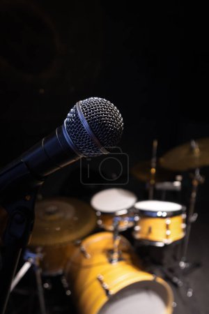 Nahaufnahme des Mikrofons vor dem Hintergrund eines verschwommenen Schlagzeugs. Vertikales Foto