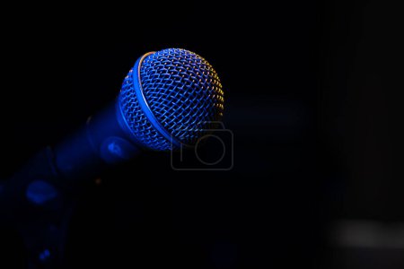 Nahaufnahme eines Mikrofons mit blauer Hintergrundbeleuchtung in einem Musikstudio, bei einem Konzert im dunklen Kopierraum