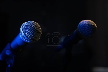 Téléchargez les photos : Gros plan de deux microphones avec rétro-éclairage bleu dans un studio de musique, lors d'un concert dans l'obscurité, copiez l'espace. Concentration sélective - en image libre de droit