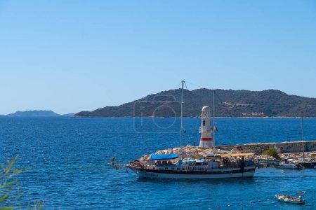 Téléchargez les photos : Kas, Turquie - 13 septembre 2023 : Yacht de fête touristique sur le fond d'un phare et les montagnes va pour une promenade en pleine mer avec les gens par une journée ensoleillée - en image libre de droit