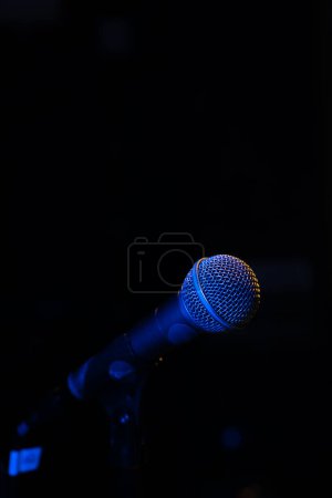 Téléchargez les photos : Gros plan d'un microphone avec rétro-éclairage bleu dans un studio de musique, lors d'un concert dans l'obscurité, copiez l'espace. Photo verticale - en image libre de droit