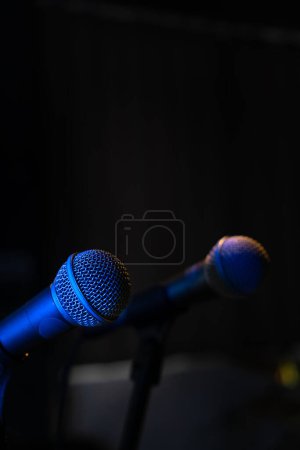 Téléchargez les photos : Gros plan de deux microphones avec rétro-éclairage bleu dans un studio de musique, lors d'un concert dans l'obscurité, copiez l'espace. Concentration sélective - en image libre de droit