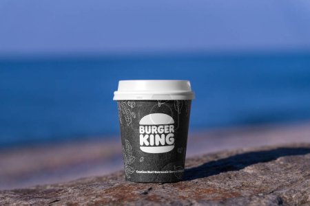 Téléchargez les photos : Batumi, Géorgie - 1 février 2024 : tasse en papier avec café ou chocolat Burger King à emporter se dresse sur une pierre sur le fond de la mer par une journée ensoleillée. - en image libre de droit