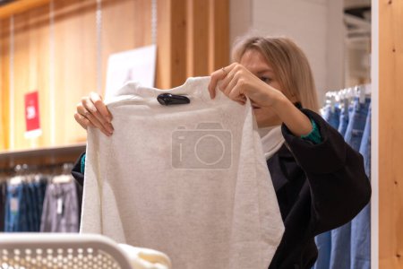 Téléchargez les photos : Jeune belle femme blonde dans un manteau choisit des vêtements dans un centre commercial - en image libre de droit