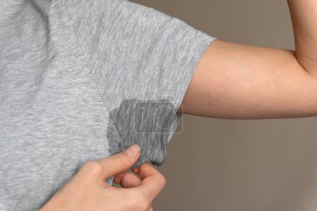Die Großaufnahme einer jungen Frau zeigt eine feuchte Achselhöhle auf einem grauen T-Shirt. Konzept Gesundheit, Sport