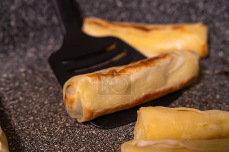 Téléchargez les photos : Gros plan du cuisinier retournant de délicieuses crêpes appétissantes avec farce dans une poêle à frire avec une spatule noire, crêpes à frire - en image libre de droit