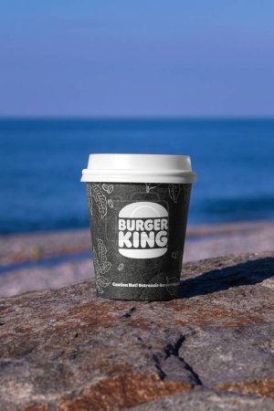 Téléchargez les photos : Batoumi, Géorgie - 1er février 2024 : tasse en papier avec café ou chocolat Burger King à emporter se dresse sur une pierre sur le fond de la mer par une journée ensoleillée. Photo verticale - en image libre de droit