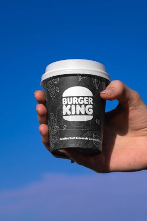 Téléchargez les photos : Batoumi, Géorgie - 1er février 2024 : Gros plan d'une main de femme tenant une tasse en papier de café Burger King sur un fond bleu ciel. Photo verticale - en image libre de droit