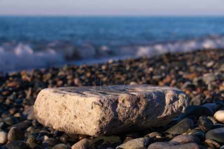 Téléchargez les photos : Gros plan d'une grande pierre plate pour insérer un objet ou un texte sur une plage de galets sur le fond de la mer par une journée ensoleillée. - en image libre de droit