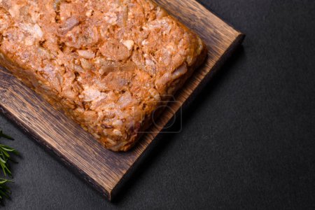 Photo for Tasty meat brawn or roll on a wooden cutting board with spices and herbs on a dark concrete background - Royalty Free Image