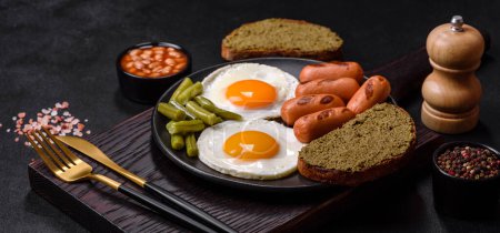 Photo for Tasty English breakfast of fried eggs, beans, asparagus, sausages with spices and herbs on a dark concrete background - Royalty Free Image