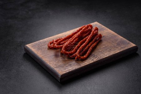 Photo for Delicious thin smoked meat sausages with spices and herbs on a dark concrete background - Royalty Free Image