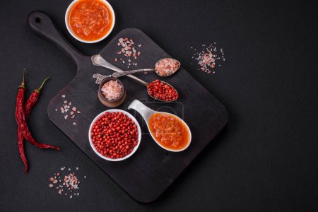 Photo for Red adjika sauce or ketchup with spices and herbs on a dark concrete background - Royalty Free Image