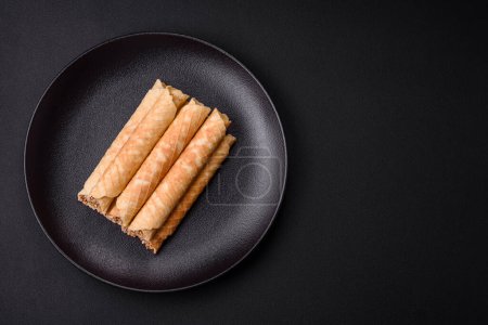 Téléchargez les photos : Délicieux rouleaux de gaufrettes croustillantes avec garniture crème aux noix sur fond de béton foncé - en image libre de droit