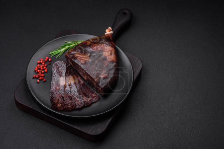 Photo for Delicious smoked or cured mahan horse meat sausage with spices and herbs on a dark concrete background - Royalty Free Image