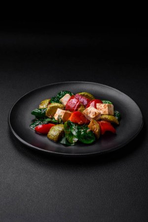 Photo for Delicious fresh salad of zucchini, cheese, sweet peppers, spinach with spices and herbs in a ceramic plate on a dark concrete background - Royalty Free Image