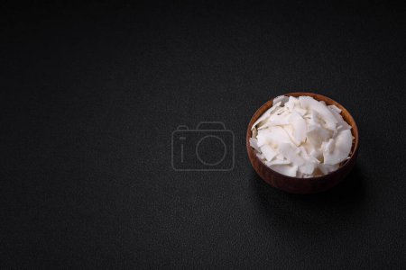 Téléchargez les photos : Flocons de noix de coco sèches blanches dans un bol en bois préparé pour faire des desserts sur un fond de béton texturé - en image libre de droit