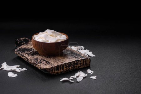 Téléchargez les photos : Flocons de noix de coco sèches blanches dans un bol en bois préparé pour faire des desserts sur un fond de béton texturé - en image libre de droit
