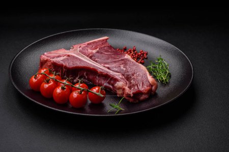 Raw juicy beef t-bone steak with salt, spices and herbs on a textured concrete background