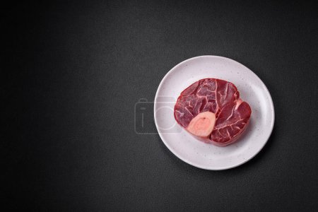 Foto de Fresh raw beef steak with bone or ossobuco with salt, spices and herbs on dark concrete background - Imagen libre de derechos