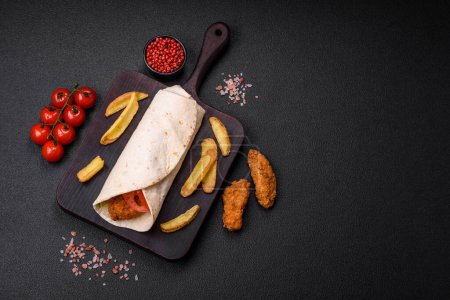 Delicious roll with chicken nuggets, tomatoes, lettuce and sauces with salt and spices on a dark concrete background-stock-photo