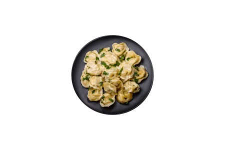 Photo for Delicious fresh dumplings with turkey meat, with spices and herbs, parsley on a black plate against a dark concrete background - Royalty Free Image