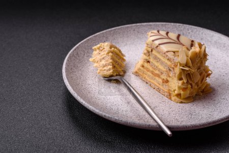 Piece of delicious sweet esterhazy cake with nuts and cream on a dark concrete background