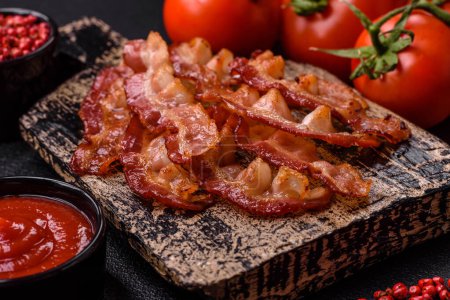Delicious fresh fried bacon with salt and spices on a dark background as an ingredient for preparing a hearty breakfast
