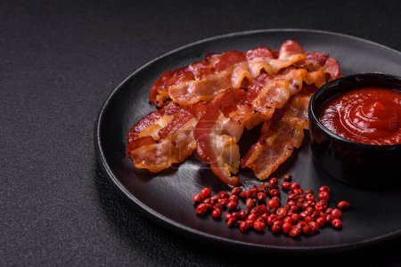 Delicious fresh fried bacon with salt and spices on a dark background as an ingredient for preparing a hearty breakfast