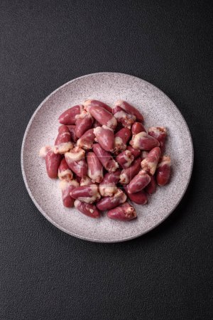 Raw chicken hearts with salt, spices and herbs on a dark concrete background