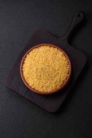 Raw anellini pasta from durum wheat with salt and spices on a dark concrete background