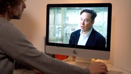 Foto de Europa, Milán 2022 - Ver las noticias de televisión en un ordenador portátil - Elon Musk entrevista - Imagen libre de derechos