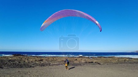 Photo for Spain, Lanzarote, Famara beach - The paraglider is the simplest and lightest means of free flight in existence - man wait for the wind in an ocean beach - Royalty Free Image